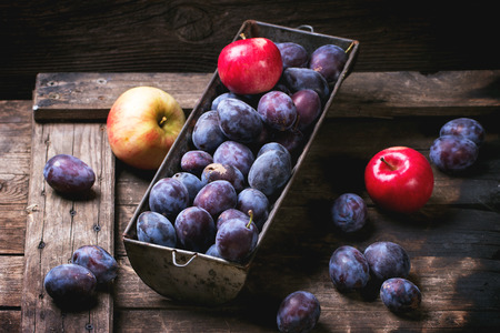 Vintage metal bowl with plums and apples over old wooden table. See sriesの写真素材