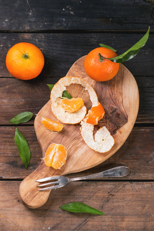 Whole and slice tangerines with leaves on olive cutting board over old wooden table. Top view.の写真素材