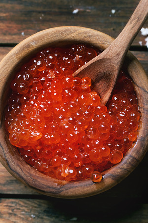 Olive wood bowl of red caviar over old wooden table. Top view.の写真素材