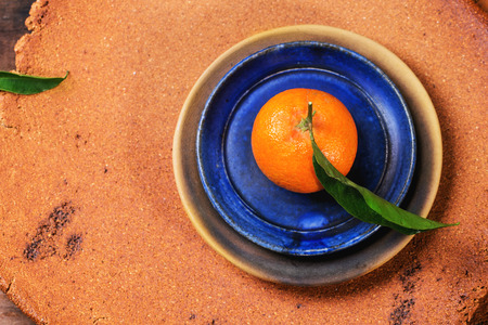 Whole tangerine with leaves on blue ceramic plate over clay tray. Top view.の写真素材