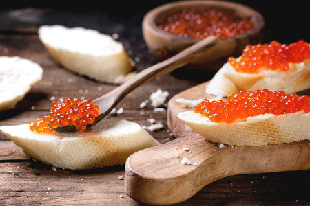 Sandwiches with red caviar served on olive wood cutting board over old wooden table. See seriesの写真素材