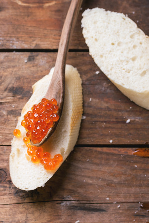 Spoon of red caviar on white bread over old wooden table. Top view. See seriesの写真素材