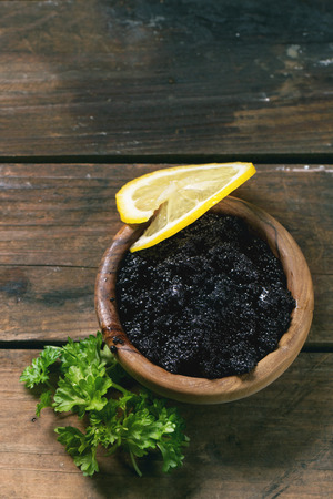 Wooden bowl of black caviar with lemon slice and parsley over old wooden table. Top view.の写真素材