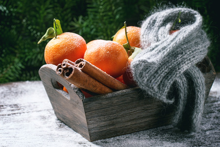 Wooden basket with tangerines, cinnamon sticks and scarf over wooden background with snow and cone.の写真素材