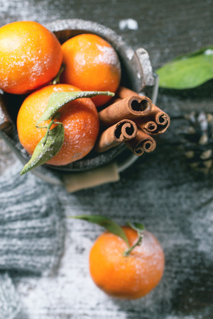 Wooden bucket with tangerines and cinnamon sticks over wooden background with snow and cone. Top view.の写真素材