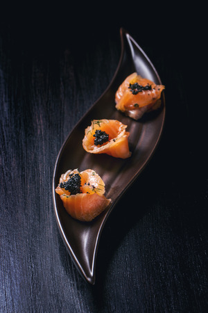Plate of salmon rolls with black caviar over black textured surfaceの写真素材