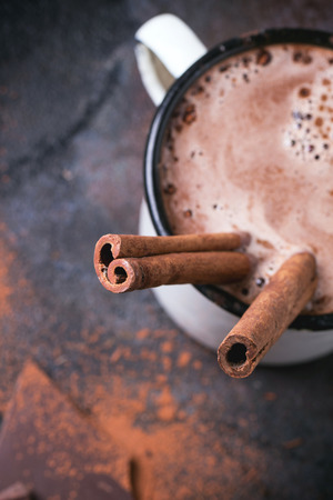 Vintage mug of hot chocolate with cinnamon sticks over dark background. Focus on cinnamon. Top view.の写真素材