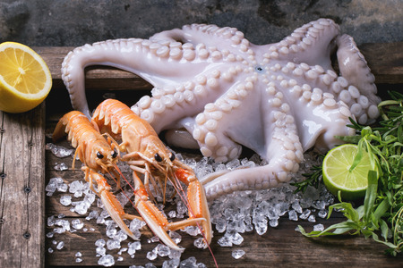 Raw octopus and langoustines on ice, served with herbs and lime over wooden tableの写真素材