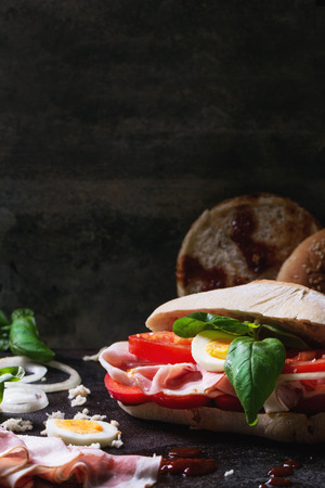 Sandwich with ham, eggs, vegetables and ketchup, served with french fries over black background. See seriesの写真素材