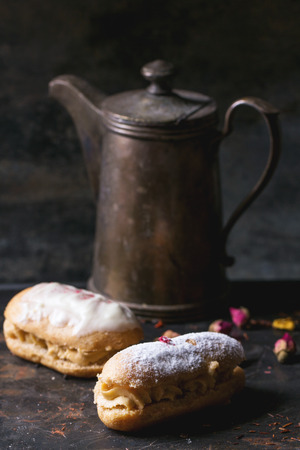 Two eclairs with white chocolate and vintage teapot over dark background.の写真素材
