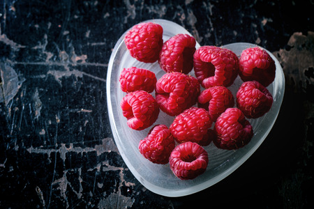 st Valentine's greeting card with fresh raspberry in heart shaped plate over black wooden background. Top viewの写真素材