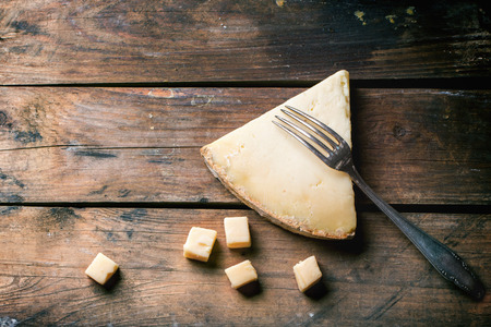 Big piece and little cubes of Belgian cheese with vintage fork over wooden background. Top view.の写真素材