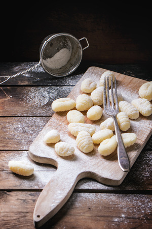 Uncooked homemade potato gnocchi with fork and strainer on vintage cutting board over wooden table with flour. See seriesの写真素材