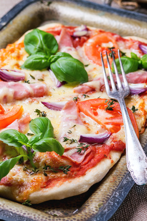 Homemade pizza with ham and tomatoes, served with fork on vintage metal tray.の写真素材