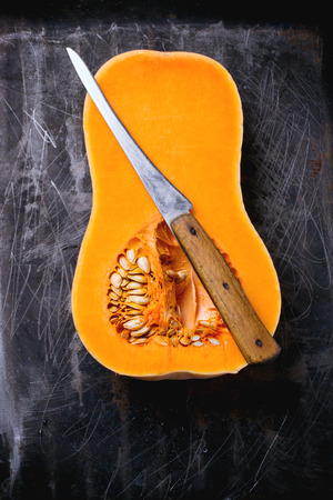 Half butternut squash with vintage knife over black metal background. Top view.の写真素材