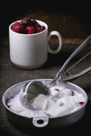 Aluminium plate with vanilla ice cream and mug of frozen berries, served with metal spoon over dark table. See seriesの写真素材