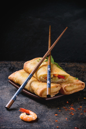 Fried spring rolls with vegetables and shrimps, served on squer ceramic plate with chopsticks over black background.の写真素材