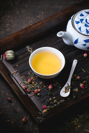 Traditional japanese teapot and cup of green tea, served on bamboo tray with dry tea variations over dark backgroundの写真素材