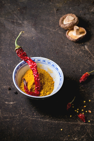 Tumeric powder in porcelain bowl, served with shiitake mushrooms and red hot chili peppers over dark table.の写真素材