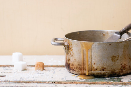 Old aluminum pan of homemade caramel sauce, served with spoons and sugar cubes over white wooden tableの写真素材