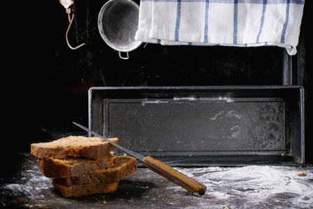 Sliced homemade rye bread over kitchen table powdered with flour, with towel, bread pan and vintage...