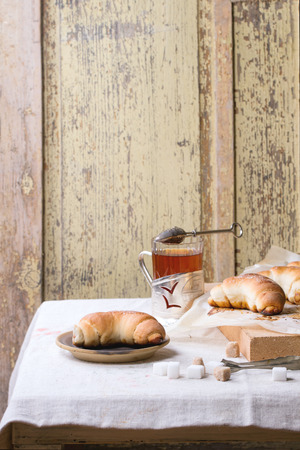 Cup of hot tea with fresh homemade baked bagels on ceramic plate and  baking paper over light gray tableclothの写真素材