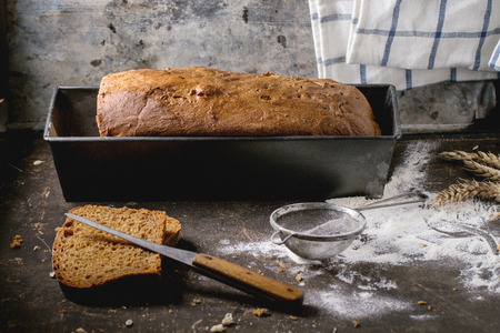 Loaf of fresh homemade rye bread with wheat seeds and flour over dark table