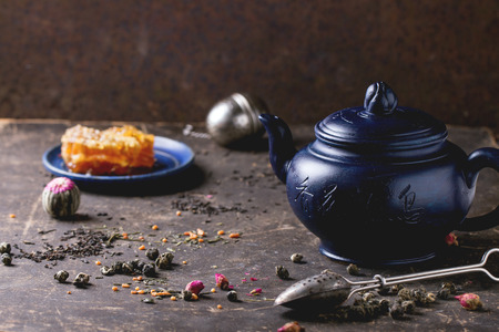 Blue ceramic teapot and plate with honeycombs, served with spoons, black and green tea lives over dark background. Chinese inscription on teapot - traditional tea drinkingの写真素材