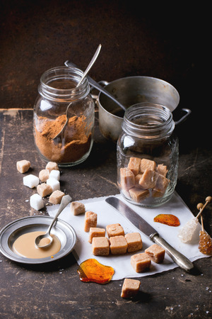 Fudge candy and caramel on baking paper and in glass jar, served over dark background with plate of caramel sauce and sugar cubes. See seriesの写真素材