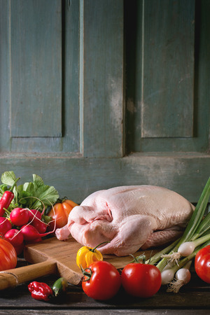 Raw young duck on wooden cutting board with fresh ripe vegetables over wooden table. Dark rustic atmosphere.の写真素材
