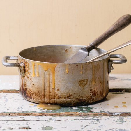 Old aluminum pan of homemade caramel sauce, served with spoons and sugar cubes over white wooden table. Selective focus, square imageの写真素材