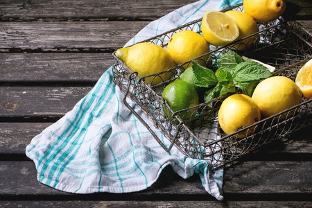 Heap of whole and sliced lemons and limes with mint in vintage metal grid box over old wooden table with turquoise wooden background. Dark rustic style.の写真素材