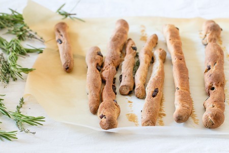 Fresh baked homemade grissini bread sticks over baking paper with rosemary herbs on white...