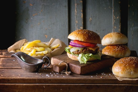 Fresh homemade burger on little cutting board with grilled potatoes, served with ketchup sauce and sea salt over wooden table with gray wooden background. Dark rustic style.の写真素材