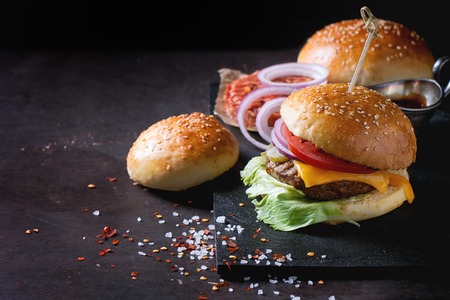 Fresh homemade burger on black slate and raw cutlet and sliced onion, served with sea salt and pepper over dark background.の写真素材