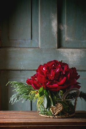Bouquet with big burgundy peonies and green bunches of thuja in vintage vase over wooden table. Dark rustic atmosphereの写真素材