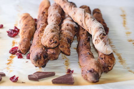 Fresh baked homemade sweet chocolate grissini bread sticks over baking paper on white tablecloth. Sun light.の写真素材