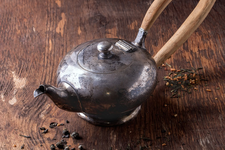Vintage metal teapot with wooden handle. With dry green tea leaves on wooden backgroundの写真素材