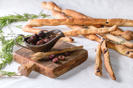 Whole and sliced black olives in vintage metal bowl with rasemary herbs and homemade grissini bread...
