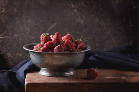 Vintage metal bowl with fresh ripe garden strawberries on wooden table with black textile. Dark rustic style. With copy space on topの写真素材