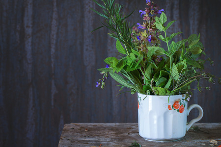 Old cup with assortment of fresh herbs mint, oregano, thym, blooming sage over old wooden background. Natural day light.の写真素材