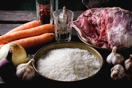 Raw ingredients for pilaf lamb, rice, carrots, onion, garlic and spices with meat backsword over wooden table. Dark rustic style.の写真素材