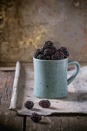 Spotted blue ceramic mug of blueberries (dewberry), at old wooden table with tin. Rustic style.の写真素材