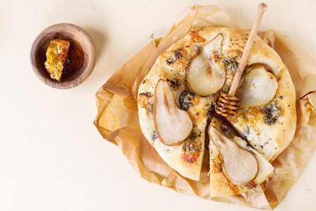 Sliced Pizza with pear, gorgonzola and honeycomb with olive wood honey dipper on baking paper over white wooden table. Top viewの写真素材
