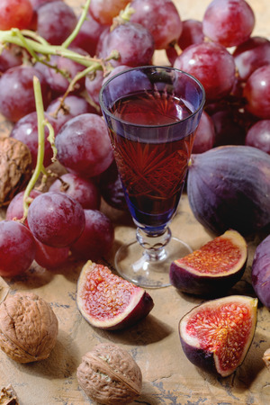 Blue vintage glass of red wine with red Grapes, Figs and Walnuts over stone surface in bright sunlight.の写真素材