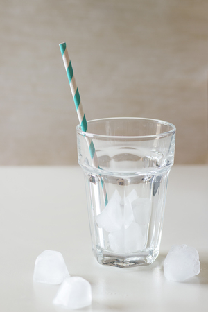 Empty cocktail glass with ice cubes and striped retro cocktail tube over white table. Natural day lightの写真素材