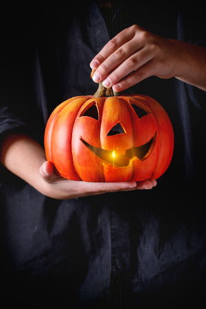 Ceramic Halloween Pumpkin lantern with burning candle in child's handsの写真素材