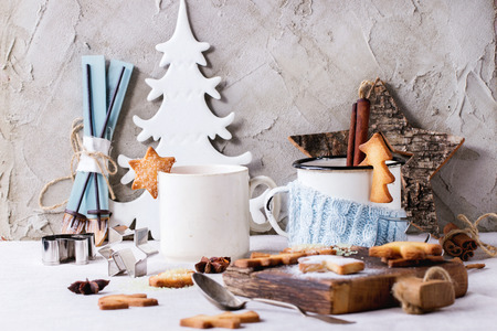 Shortbread Christmas cookies for cups, two cups of hot tea and sugar powder over table with white tablecloth with Christmas decor at background. Shapes as Christmas tree, stars and Santa Claus Hatの写真素材