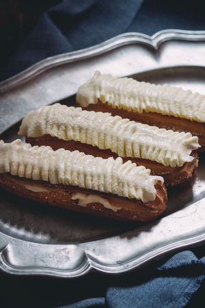 Home made Eclairs with white butter cream in vintage metal plate. Dark rustic style. Day light. Outside viewの写真素材