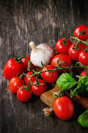 Assortment of colorful cherry tomatoes with garlic and basi on small cutting board over old wooden table.の写真素材